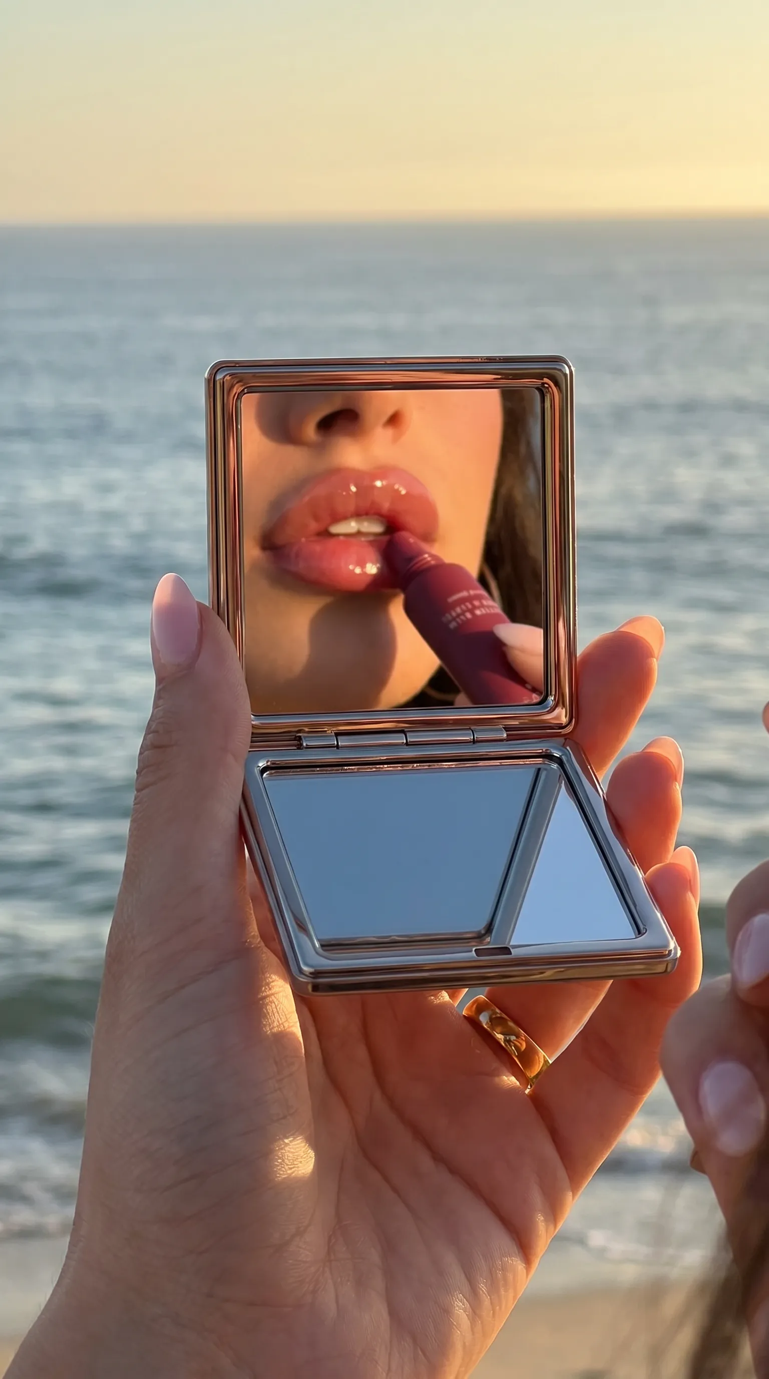 Cherry Lip Butter Balm reflected in a compact mirror by the ocean