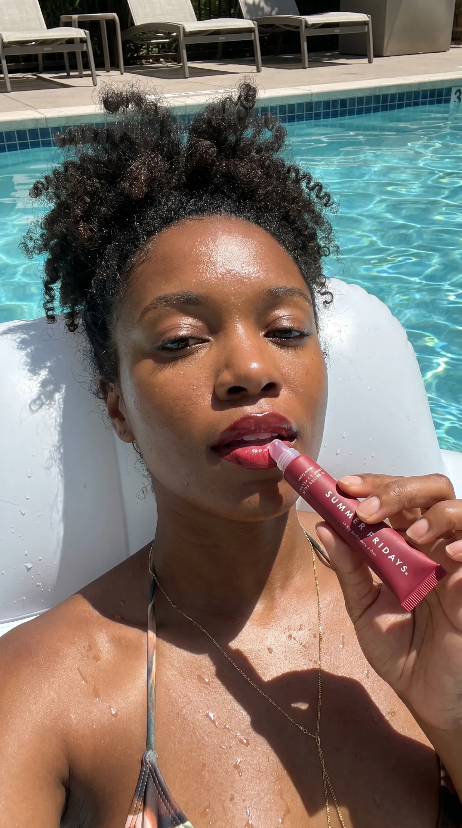 Person applying the connected cherry Lip Butter Balm beside a swimming pool
