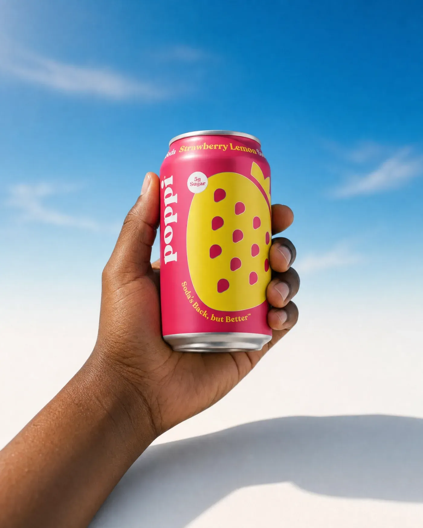 Hand holding a pink strawberry lemon soda can against a blue sky