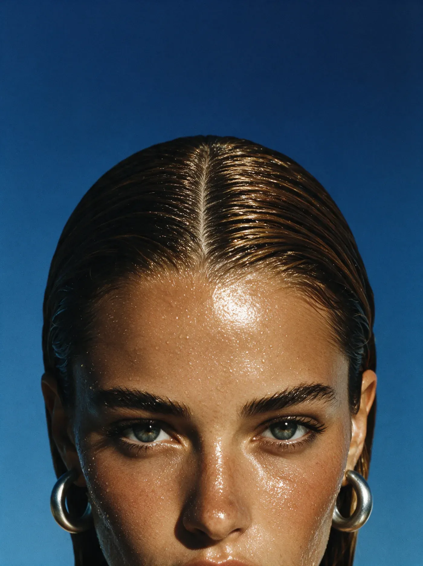 Close-up portrait wearing silver hoop earrings against a blue background
