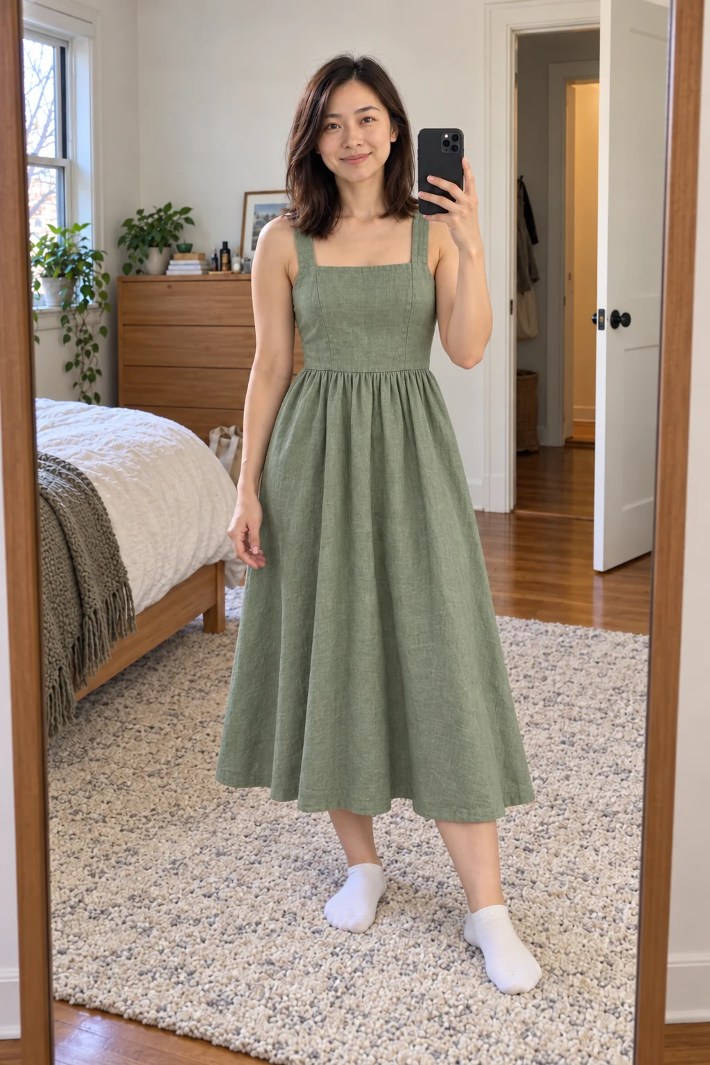 The same mirror selfie with Maya wearing the sage linen dress, keeping her pose, phone and room